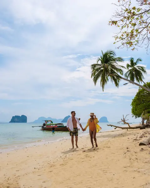 Happy young couple, an Asian woman and European man on the beach of Koh Ngai island, soft white sand, and a turqouse colored ocean in Koh Ngai Trang Thailand