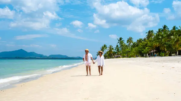 一对年轻的高加索男人和一个泰国亚洲女人在热带岛屿高目岛的海滩上散步 他们的棕榈树是柔软的白沙滩 而在泰国的高目岛则是一片草屋色的海洋 — 图库照片