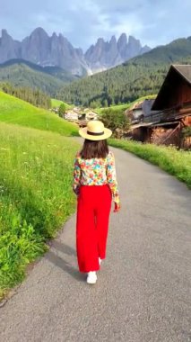 Dolomites İtalya 'daki Santa Maddalena Köyü' nün manzarasını görmek için vadideki köyde yürüyen şapkalı Asyalı kadın, Santa Magdalena köyü Dolomites dağları, Val di Funes vadisi İtalya