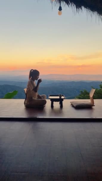 日没の山で紅茶を飲むアジア人女性 北タイの休暇の和風ホームステイで チェンライ チャンの山のホームステイ小屋に滞在 — ストック動画