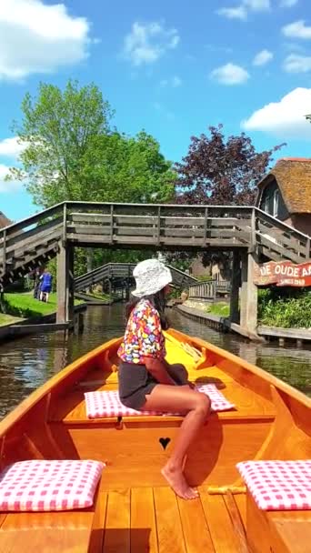 Giethoorn Netherlandsの運河で木製のボートで帽子をかぶったアジアの女性 ボートの観光客は春の日に農場のエリアで屋根の家を焼いたカナルや素朴な村を訪問 — ストック動画