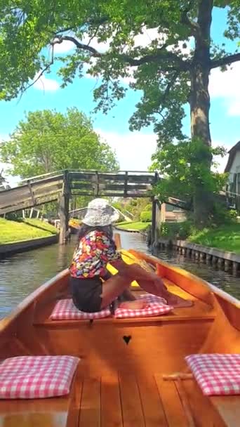 Giethoorn Netherlandsの運河で木製のボートで帽子をかぶったアジアの女性 ボートの観光客は春の日に農場のエリアで屋根の家を焼いたカナルや素朴な村を訪問 — ストック動画