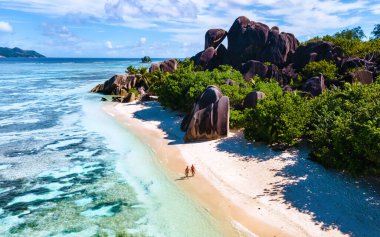 Anse Source d 'Argent plajı, La Digue Adası, Seyshelles, La Digue Seychelles kuş bakışı hava aracı manzaralı tropikal adayı, günbatımında sahilde yürüyen iki erkek ve kadın.