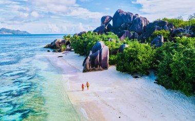 Anse Source d 'Argent plajı, La Digue Adası, Seyshelles, La Digue Seychelles kuş bakışı hava aracı manzaralı tropikal adayı, günbatımında sahilde yürüyen iki erkek ve kadın.
