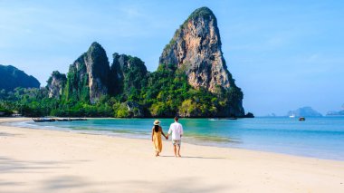Tayland Railay Beach Krabi 'de tatilde plajda dinlenen ve arka planda güzel kireçtaşı kayalıkları olan bir çift kadın ve erkek.
