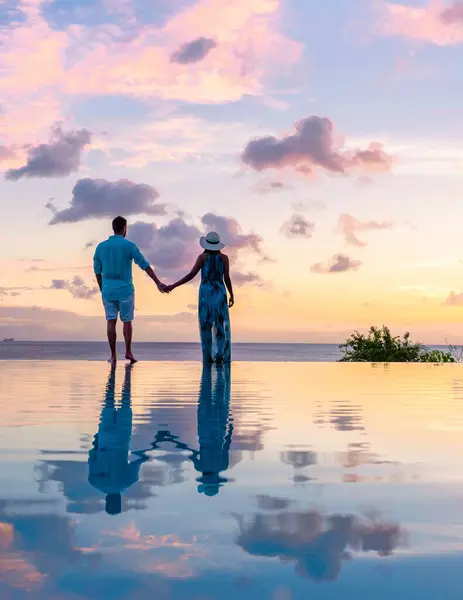 men and women watching the sunset with reflection in the infinity swimming pool at Saint Lucia Caribbean, couple at infinity pool during sunset on a tropical island during summer holiday vacation