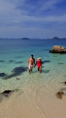 Kumsalda çeşitli gezintiler, erkekler kadınların elinde gezintiler. Su berrak gökyüzünün altında parıldıyor, kabarık bulutlar üzerinde sürükleniyor, Ko Kham Tayland