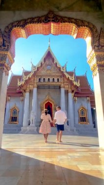 Bir çift görkemli bir tapınağın önünde el ele tutuşuyorlar. Binanın mimarisi, Bangkok Tayland 'daki Wat Benchamabophit tapınağı ile simetriktir.