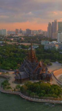 Bir park ve suyla çevrili bir gökdelenin havadan görünüşü, doğal manzara ile kentsel tasarımı harmanlıyor, alacakaranlık gökyüzüne karşı, Pattaya, Doğruluk Tapınağı, Tayland