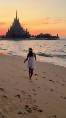 Asyalı bir kadın gün batımında sahilde geziniyor, çarpan dalgaların, renkli gökyüzünün, Hakikat Tahta Tapınağı Pattaya Tayland Sığınağı 'nın huzurlu atmosferinin tadını çıkarıyor.