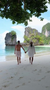 Kumsalda el ele gezen bir çift, açık mavi gökyüzü altında kıyıya vuran dalgaların seslerinin tadını çıkarıyorlar Koh Hong Adası Krabi Tayland