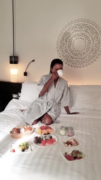 一个女人坐在一张床上 床上放着一盘盘盘的食物 卧室里铺着纺织品亚麻布 房间装潢美观 氛围舒适 — 图库视频影像