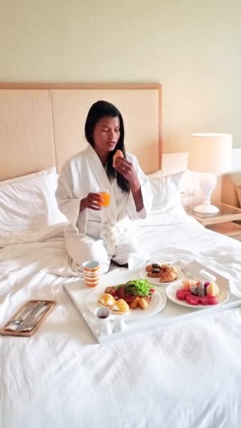 一个女人拿着一盘食物坐在床上 展示着各种餐具和餐具 她的盘子里有一道美味的菜肴 可以在床上享用 — 图库视频影像