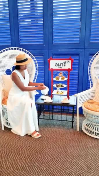 見事な白い結婚式のガウンと電気ブルーの帽子の女性は タイのホアヒン公式イベントでピーコックチェアの上にエレガントに座っています — ストック動画