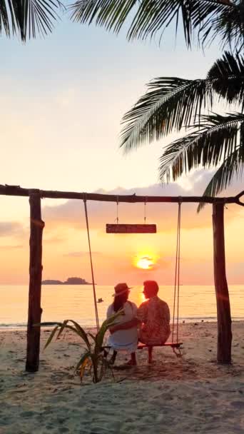 Ζευγάρι Απολαμβάνει Ηλιοβασίλεμα Μια Κούνια Στην Παραλία Που Περιβάλλεται Από — Αρχείο Βίντεο