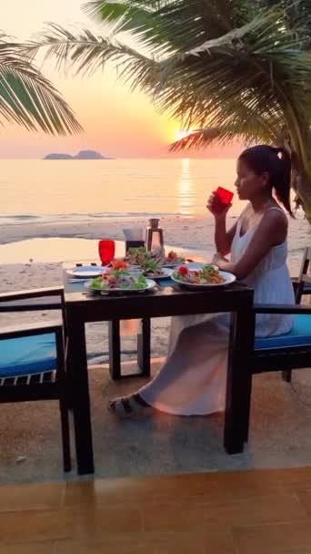 Μια Γυναίκα Κάθεται Ένα Ξύλινο Τραπέζι Θέα Ηλιοβασίλεμα Στον Ωκεανό — Αρχείο Βίντεο