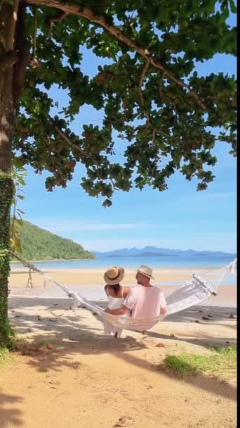 Para Relaksuje Się Hamaku Plaży Otoczona Wodą Niebem Drzewami Trawą — Wideo stockowe