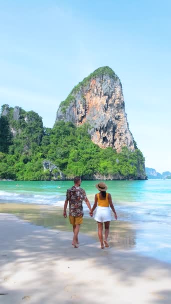 ビーチを散策するカップルは 木の自然の風景に囲まれた手を握ります ショートパンツの他の人々は タイのクラビーチ ライレイビーチの美しい景色を楽しんでいます — ストック動画