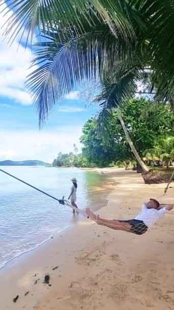 남자는 파도의 진정한 소리와 풍경의 아름다움으로 둘러싸인 해변에 해먹에서 Lounging — 비디오