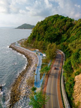 Tayland 'ın okyanus sahil yolu boyunca virajlı yolda giden araba. Yazın yol manzarası. Sahildeki otoyolda araba kullanmak çok güzel. Chantaburi Eyaleti Tayland Gün batımında
