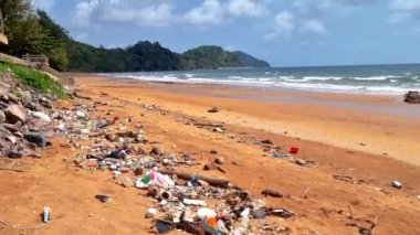 Kumsala çöp döküldü, boş plastik şişeler kullanıldı. Kirli deniz kumlu kıyı, çevresel kirlilik ekolojik sorunlar Chantaburi Tayland 'da dalgaların arka planda taşınması
