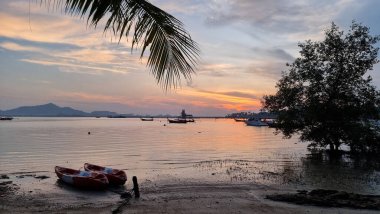 Renkli bir tekne güneşli bir günde kumlu bir sahilde, altın taneciklerle çevrili ve açık mavi bir gökyüzünün altında boş boş oturuyor. Koh Mook Tayland 