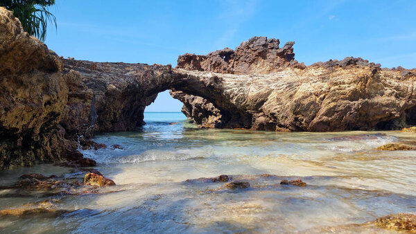 A rocky beach with a small arch standing in the middle, framing the scenic view of the surrounding seascape. Koh Libong Thailand 