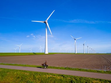 Baharda Hollanda Flevoland 'da güneşli bir günde rüzgâr türbinlerinin yanında toprak bir yolda elektrikli bisiklete binen bir adam. Kırsal kesimde elektrikli bisiklet süren erkekler