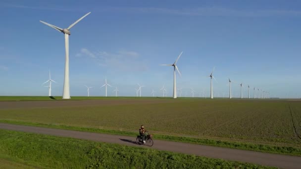 在荷兰的一个美丽而明亮的日子里 一个骑着绿色电动车的男人骑着一辆风车在一个风车农场的涡轮机旁骑着一辆绿色电动车 — 图库视频影像