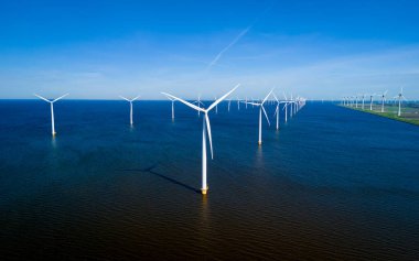 Hollanda 'nın Flevoland kıyılarında, okyanus esintisinde zarif bir şekilde sallanan bir sıra rüzgar türbininin büyüleyici hava görüntüsü. Yel değirmeni türbinleri enerji geçişi yapıyor