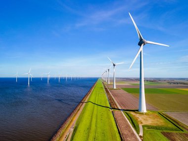 Hollanda 'nın göbeğinde sakin bir sahne, canlı bahar mevsiminde, bir sıra rüzgâr türbini, huzurlu bir su kütlesinin yanında zarifçe dönüyor. enerji geçişi