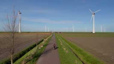 Netherlands Flevoland Noordoostpolder 'da güzel, parlak bir günde yel değirmeni yel değirmeninin yanında bisiklet süren genç bir adam yeşil bir elektrikli bisikletle kırsal alanda bisiklet sürüyor.