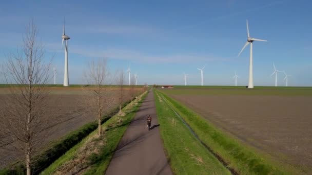 在荷兰的一个美丽的阳光灿烂的日子里 一个骑着绿色电动车的年轻人被一个风车农场的风车隔离了 男人骑着绿色电动车在乡间骑车 — 图库视频影像