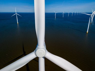 Yel değirmeni türbinlerinin sıralarının okyanusun engin genişliğinde zarifçe döndüğü bir rüzgar çiftliğinin havadan görüntüsü, Hollanda Flevoland 'da canlı bahar mevsiminde çekildi..