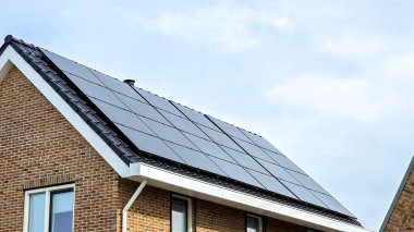 Çatıda siyah güneş panelleri olan yeni yapılmış evler güneşli bir gökyüzüne karşı siyah güneş panelleri olan yeni binaları kapatıyorlar. Zonnepanelen, Zonne Energie, Çeviri: Güneş Paneli, Güneş Enerjisi