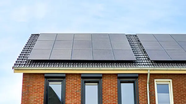 晴れた空に向かって屋根に黒い太陽電池パネルが付いている新しい家黒い太陽電池パネルは黒い太陽電池パネルが付いている新しい建物の近くに Zonnepanelen ゾンヌーニャ ソーラーパネル 太陽エネルギー ストック写真