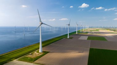 Hollanda, Flevoland 'daki bir rüzgar çiftliğinin büyüleyici hava manzarası. Yel değirmeni türbinlerinin ritmik olarak okyanus yakınlarında temiz enerji ürettiği yer..