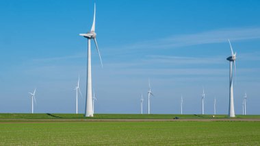 Huzurlu yeşil çimenler önümüzde uzanır, arkaplanda zarif bir şekilde dönen görkemli yel değirmenleri koleksiyonu ile benekli..