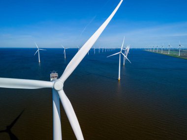 Hollanda Flevoland bölgesinden bir grup pitoresk yel değirmeni güzel bir bahar gününde sakin bir su kütlesinin üzerinde zarifçe süzülür. Yel değirmeni türbinleri okyanustaki yeşil enerjiyi