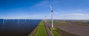 A stunning view of a row of wind turbines gracefully turning along the horizon of a vast body of water in Flevoland, Netherlands during the vibrant season of Spring. clipart