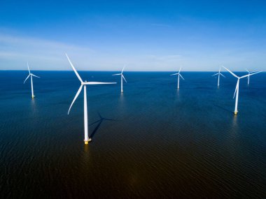 Bir grup rüzgâr türbini okyanusta dimdik ayakta duruyor. Rüzgarın gücünü kullanarak Hollanda Flevoland 'da canlı bahar mevsiminde yenilenebilir enerji üretiyorlar..