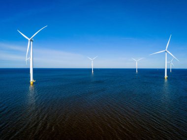 Bir grup rüzgâr türbini, canlı bahar mevsiminde Hollanda Flevoland 'daki okyanus yüzeyinde zarifçe dönüyor. Yel değirmeni türbinlerinin insansız hava görüntüsü yeşil enerji 