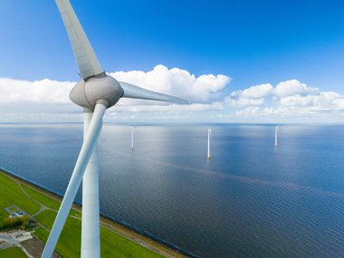A single wind turbine towers over the ocean, its blades spinning gracefully in the wind, harnessing the power of nature in the picturesque setting of the Netherlands in Spring. clipart