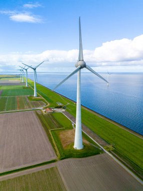 Yükselen türbinlerden oluşan bir rüzgar çiftliği, büyük bir su kütlesinin ortasında zarifçe duruyor. Baharda Hollanda 'da sakin ve sürdürülebilir bir manzara. Flevoland 'da bir sıra yel değirmeni türbini