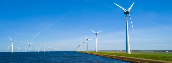 stock image A serene scene in the Netherlands Flevoland, with a picturesque row of wind turbines gracefully spinning next to a tranquil body of water on a sunny Spring day. windmill turbines green energy