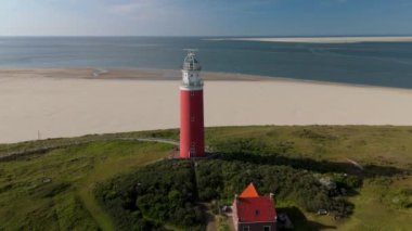 Hollanda Hollanda Hollanda 'daki Texel kırmızı deniz fenerinde Wadden Adası' nda kum tepeleri var. Kumsalın yukarısından drone hava görüntüsü ve okyanusta gün batımı.
