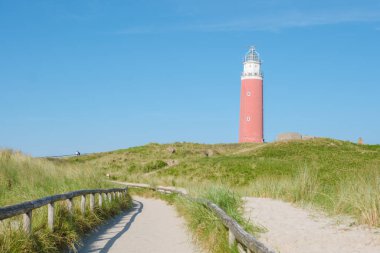 Kumların arasından geçen dolambaçlı bir yol mavi gökyüzüne karşı dimdik duran görkemli bir deniz fenerine çıkar. Kayıp denizcilere yol gösterir. Teksas Hollanda 'nın ikonik kırmızı deniz feneri.