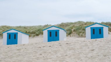 Teksas, Hollanda 'nın kumlu sahillerinde kendine özgü mavi kapıları olan üç büyüleyici sahil kulübesi duruyor..