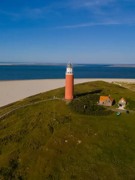 stock image A majestic lighthouse stands tall on a green hill in Texel, Netherlands, guiding ships safely with its powerful beacon.