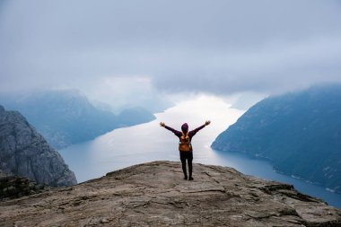 Norveç 'in ünlü Preikestolen uçurumunun kenarında kollarını açmış yalnız bir yürüyüşçü, çarpıcı bir fiyorda ve çevresindeki dağlara tepeden bakıyor. Norveç, Preikestolen